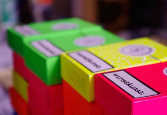 In neon Farben gestapelte Schachteln. Oben drauf der schwarze Schriftzug Wunstkunst auf weißem Grund.