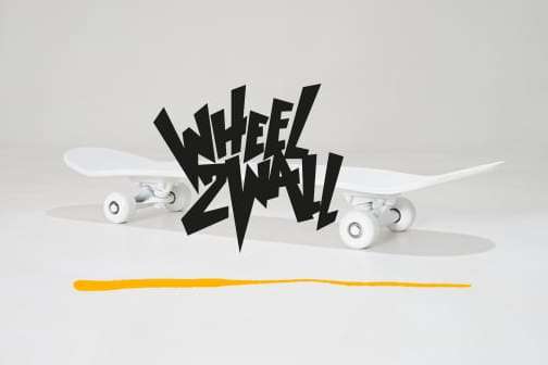 schwarzer Wheel2Wall Schriftzug vor weißem Skateboard, unterstrichen von gelben Strich.