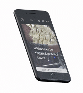 Ein animiertes, schwebendes Smartphone, das sich leicht hin und her neigt. Auf dem Display ist die mobile Startseite des „G-Class Experience Center“ mit dem Begrüßungstext und einem „JETZT BUCHEN“-Button zu sehen.