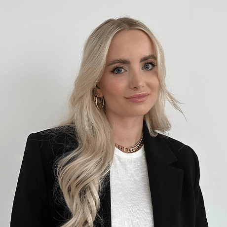 Portrait von Kim Engelage, Mitarbeiterin von Knorke Media. Sie trägt ein weiß meliertes Oberteil mit einem schwarzen Blazer.