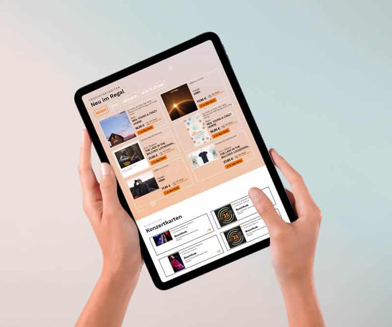 Schwarzes Tablet gehalten von zwei H&auml;nden. Auf dem Bildschirm die Website von Buschfunk. Der Hintergrund rosa zu hellblau verlaufend.