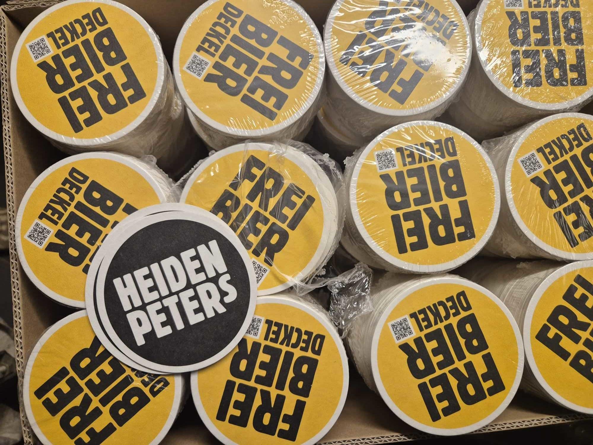Karton voll mit runden gelben Bierdeckeln. In schwarz darauf: